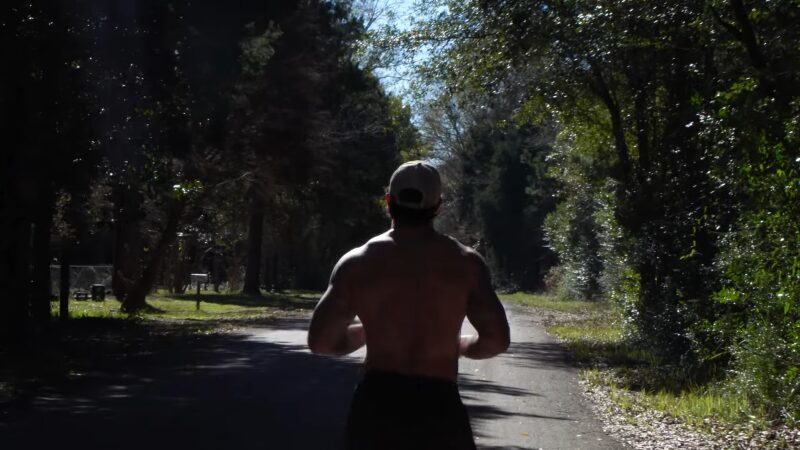 A Shirtless Man Jogs Along a Forested Road, Likely Participating in A Military Running Program Aimed at Enhancing Endurance and Strength