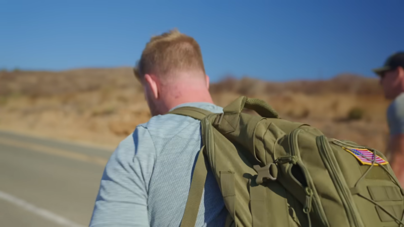 A Man with A Military-Style Backpack Participates in A Ruck Run on A Dry, Open Road Under a Clear Blue Sky, Symbolizing Tactical Fitness and Endurance