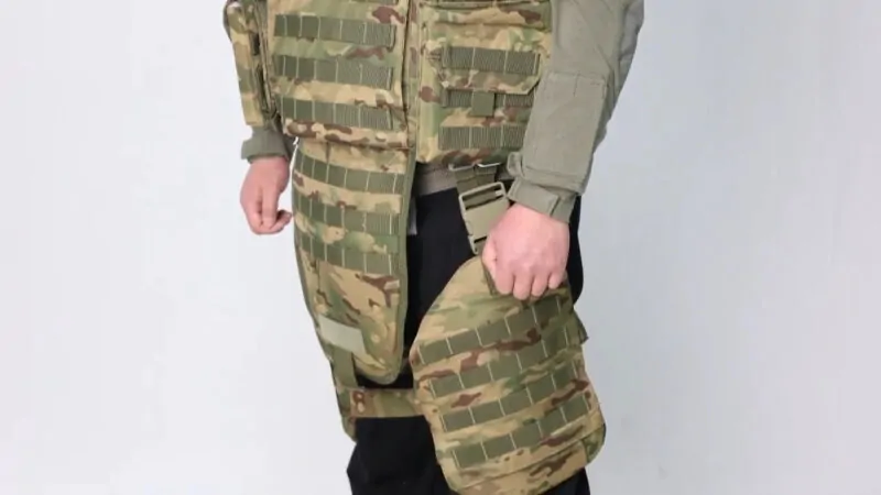 Person wearing a camouflaged bulletproof vest, showing the vest's details and design, set against a plain background to highlight the body armor