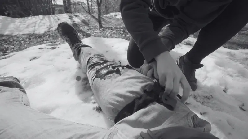 A Person Providing Gunshot Wound Care by Applying a Tourniquet to Stop Bleeding on The Leg of An Injured Individual