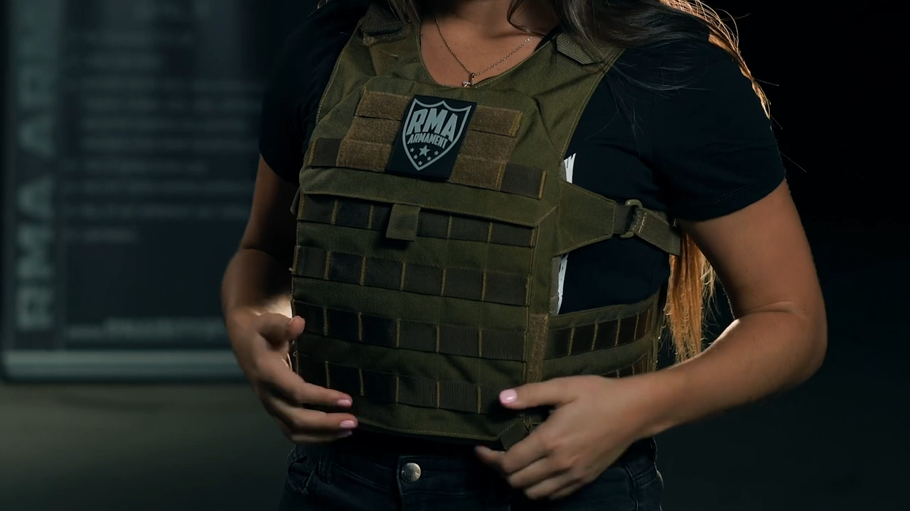 Woman adjusting a green bulletproof vest with an RMA Armament logo, showcasing the vest's features and design