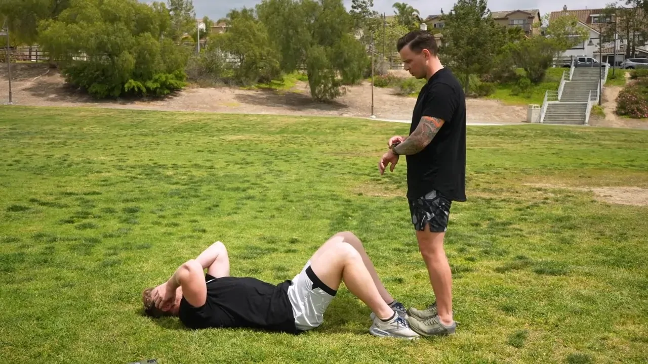 Guy attempting the Coast Guard Fitness Test on green grass while another man is helping him