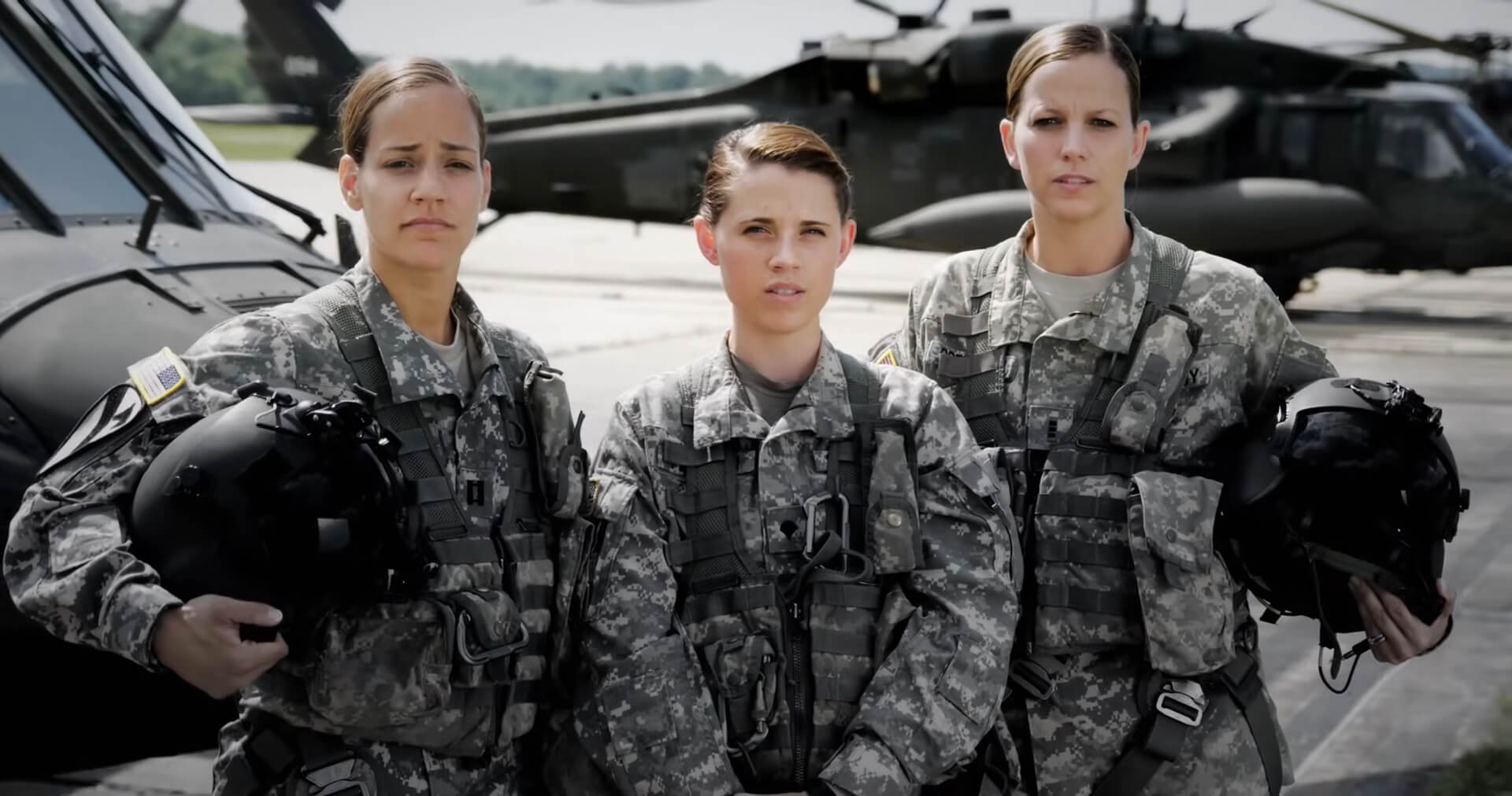 Three military personnel in uniform standing in front of helicopters