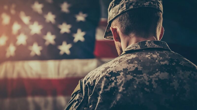 A rear view of a soldier in military uniform, looking towards an American flag, symbolizing patriotism and commitment