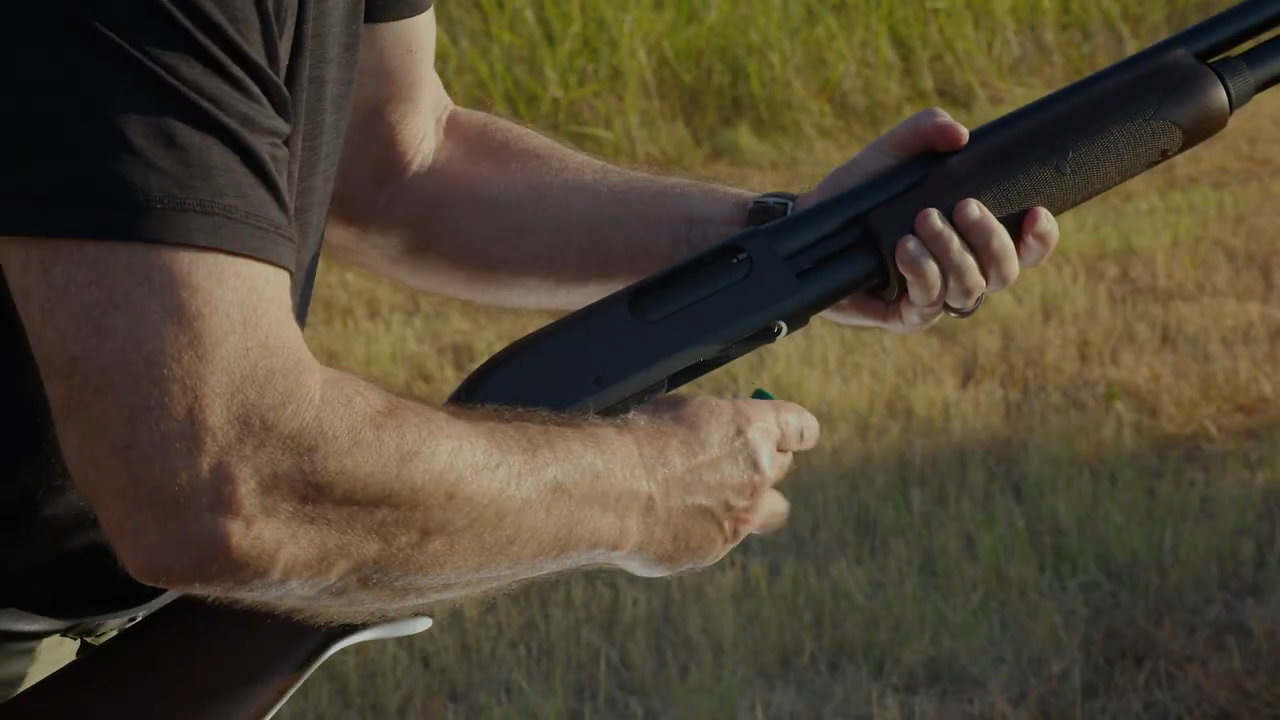 person loading a shell into a Remington 870 pump-action shotgun outdoors