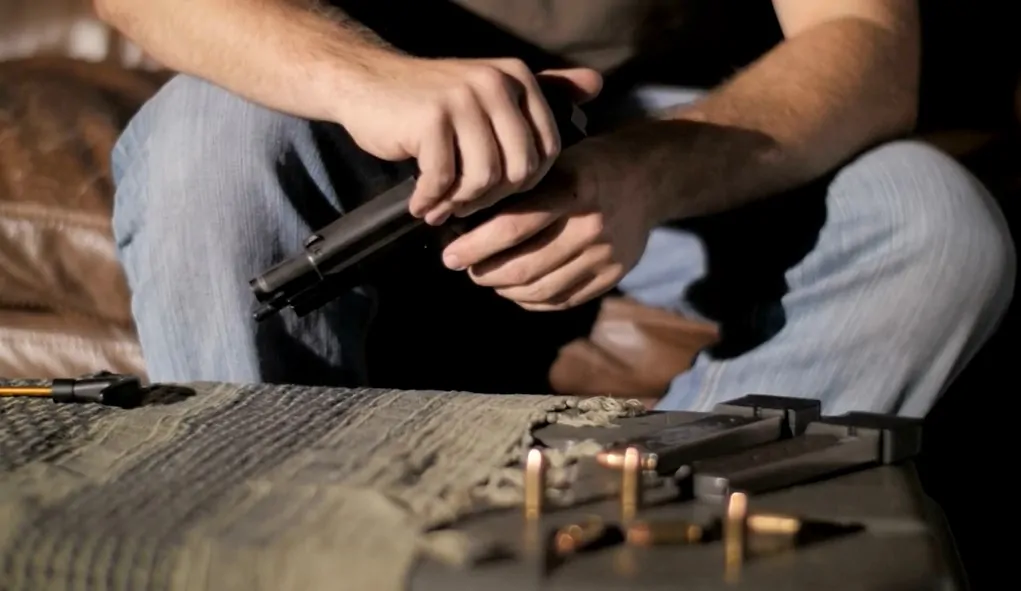 Man holding a gun and bullets are on the table in front of him