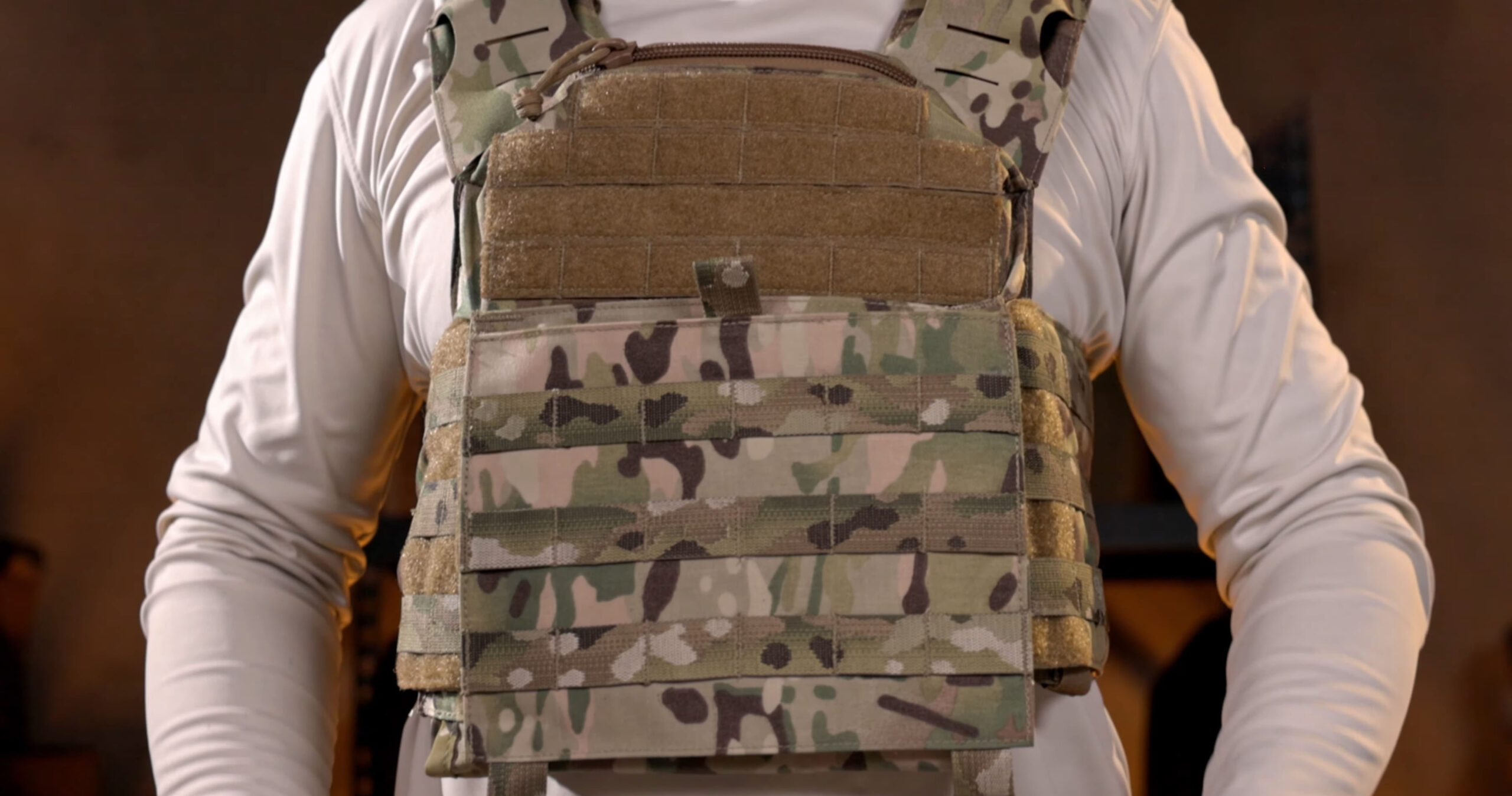 Close-up of a camo-patterned tactical plate carrier worn over a white shirt, with "Body Armor 101" text branding in the corner