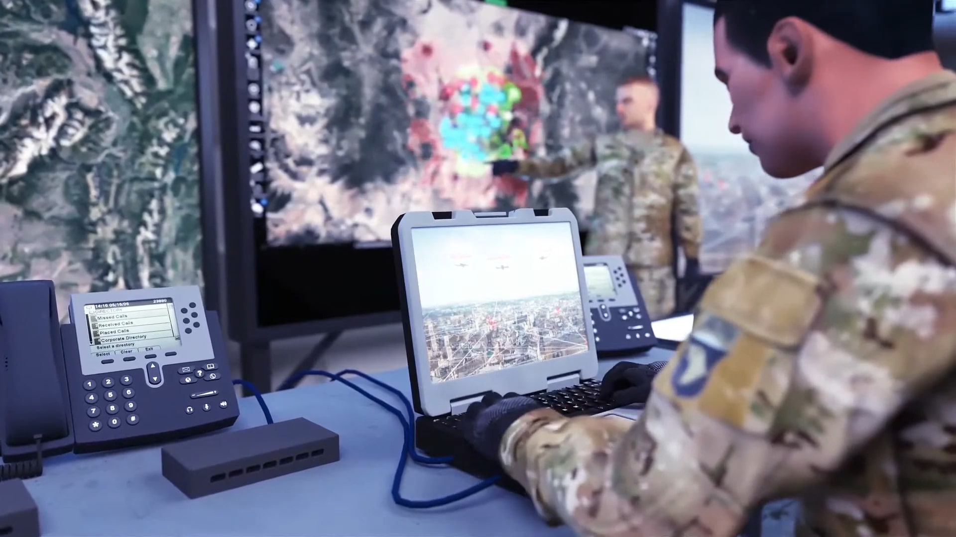 Military personnel working in a command center with computers and large digital maps