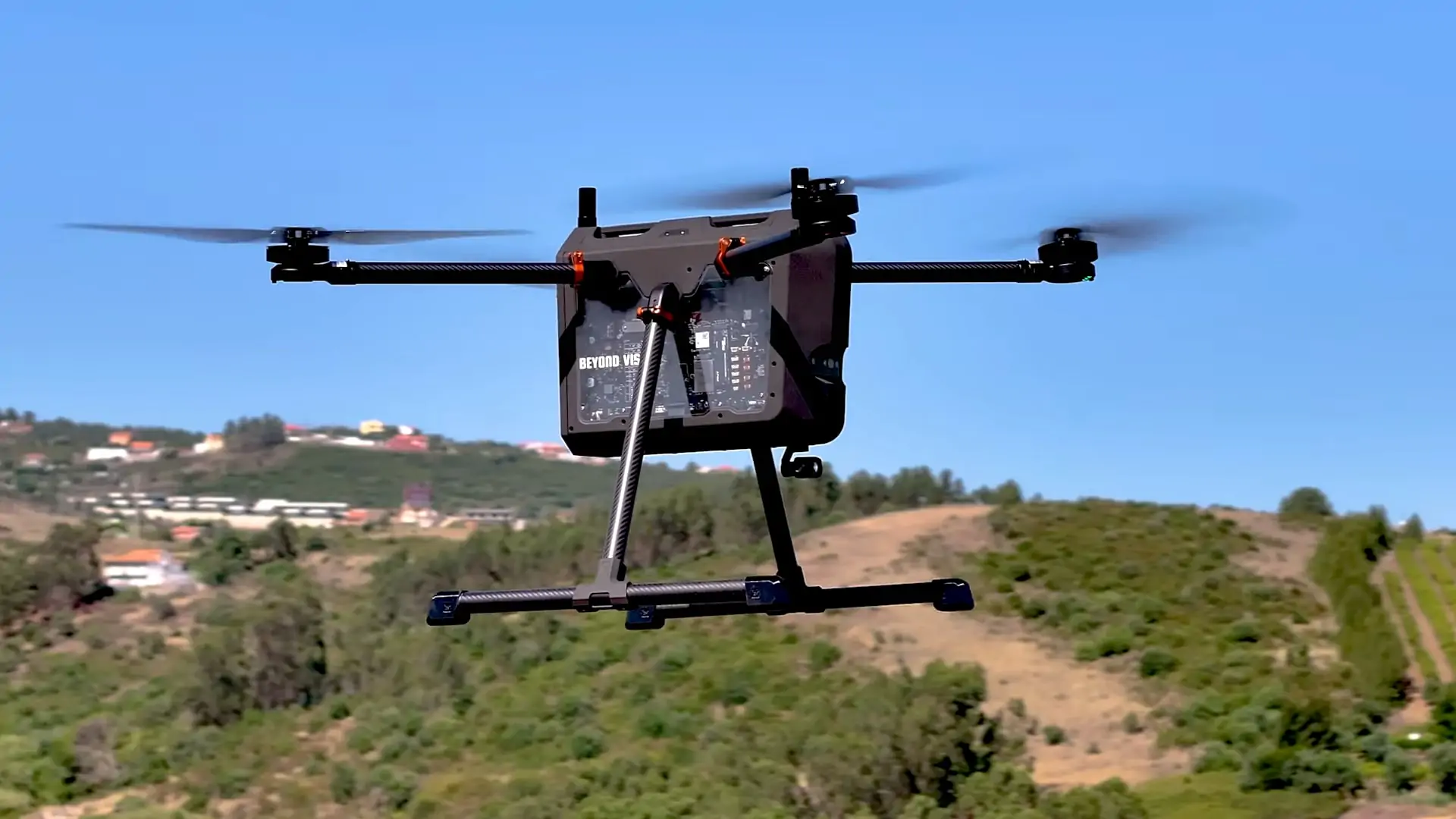 Quadcopter UAV in flight over a rural area with hills and houses in the background