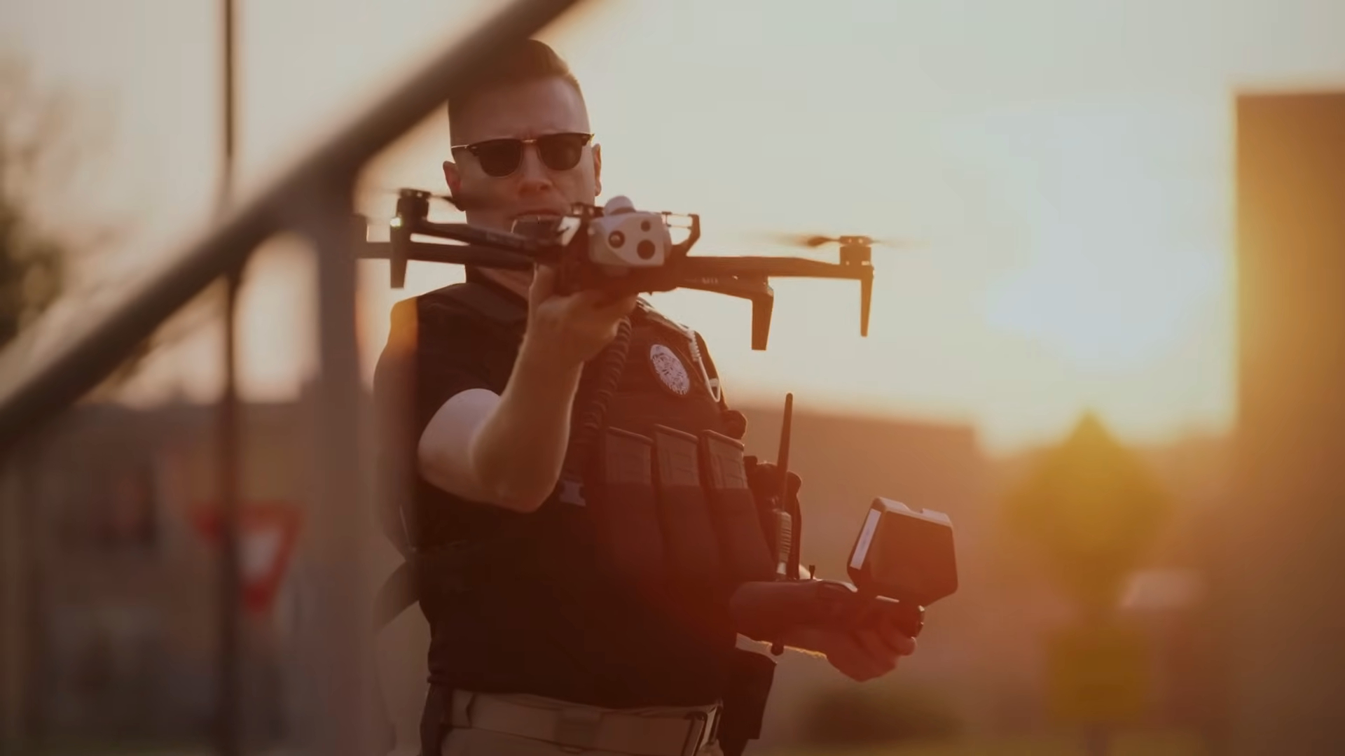 A police officer holding a drone and a controller, preparing for deployment at sunset