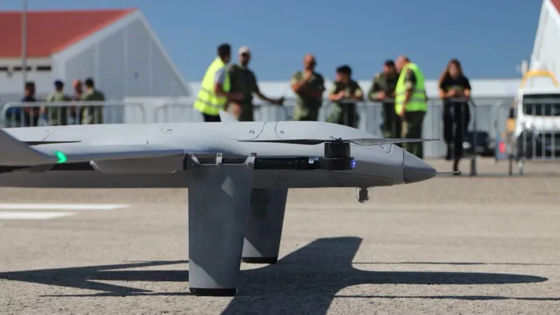 Close-up of a UAV on the ground with a military team in the background during a demonstration