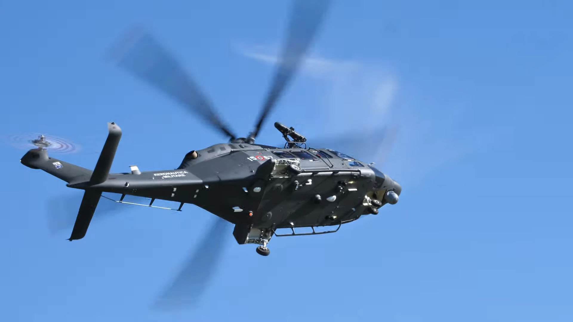 A black helicopter in flight against a bright blue sky, equipped with advanced instrumentation