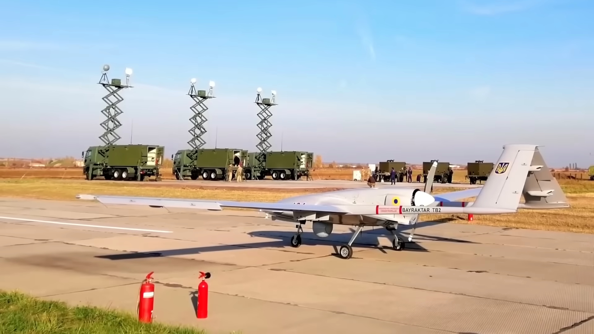 A Bayraktar TB2 drone stationed on an airstrip with military radar vehicles in the background