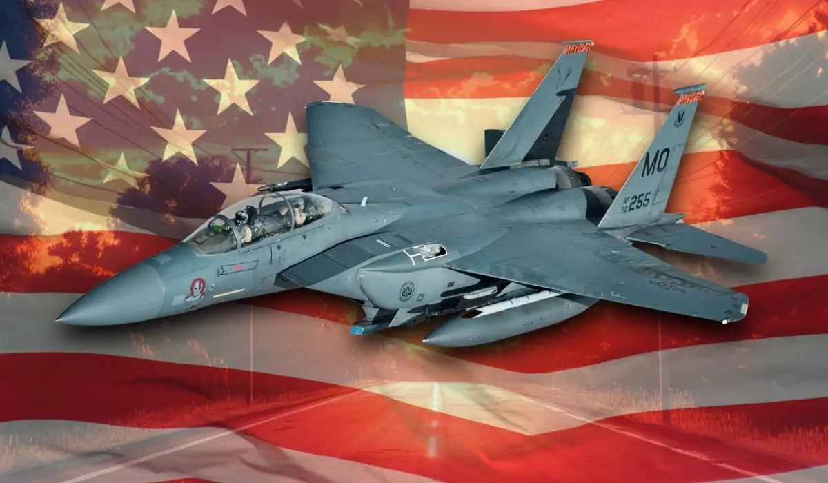 An American F-15 Eagle fighter jet with twin vertical stabilizers, flying over a background featuring the U.S. flag