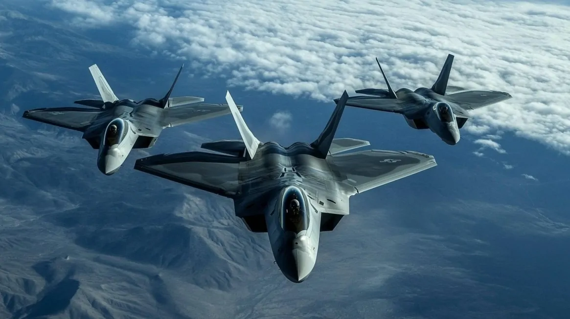 Three F-22 Raptor fighter jets flying in tight formation over a mountainous landscape with clouds in the background