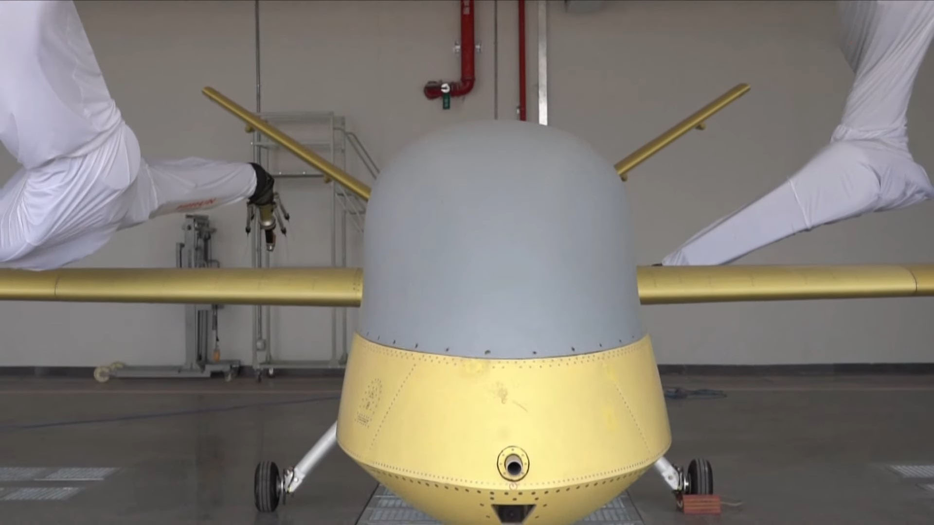 Front view of a Wing Loong II UAV inside a hangar, partially covered, with its wings and components being assembled